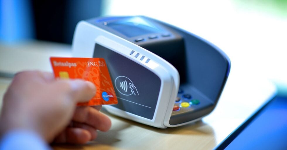 Close-up of a hand tapping an orange card against a card reader for contactless payment.