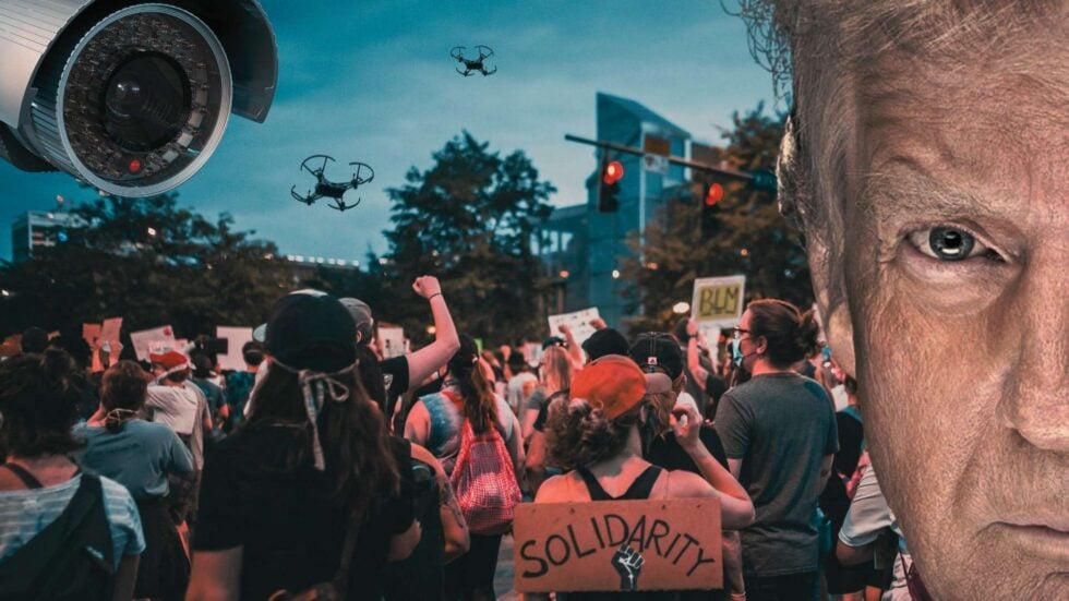 Protestujący tłum widziany od tyłu, widoczna tabliczka z napisem "Solidarity", na niebie w lewym górnym rogu kamaera inwigilijąca i dwa drony, po prawej stronie połowa twarzy Trumpa