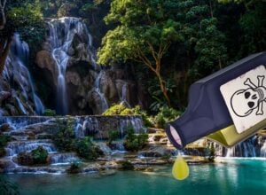 Tall forest waterfall with a large tilted device displaying a skull-and-bones warning, leaking a yellow drop into a clear pool