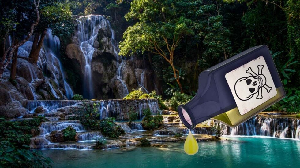 Tall forest waterfall with a large tilted device displaying a skull-and-bones warning, leaking a yellow drop into a clear pool