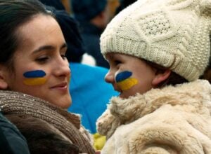 Two people facing each other with blue and yellow face paint, wearing warm coats and a cream knit hat on one side.
