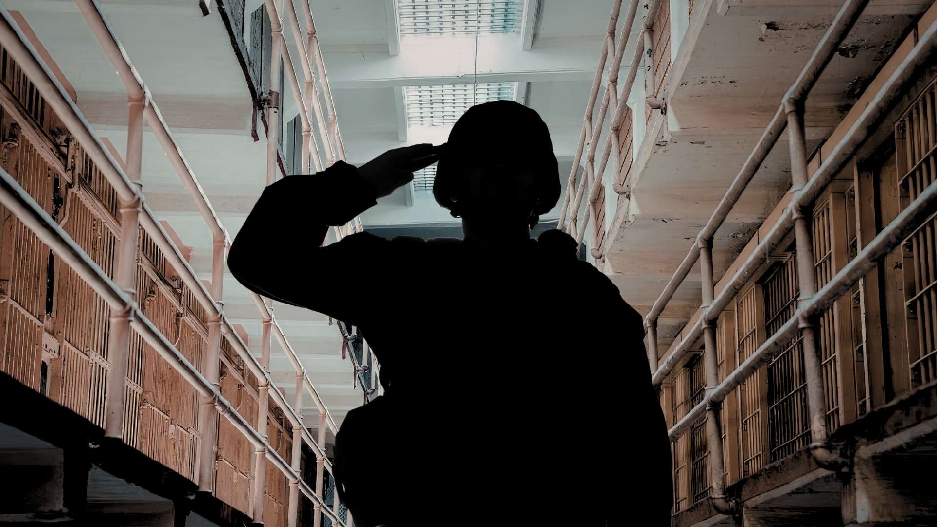 Silhouette of a person saluting in a prison corridor with barred cell doors on both sides perhaps a hallway.