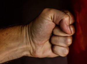 Close-up of a clenched fist against a dark background with a red fabric edge on the right side.