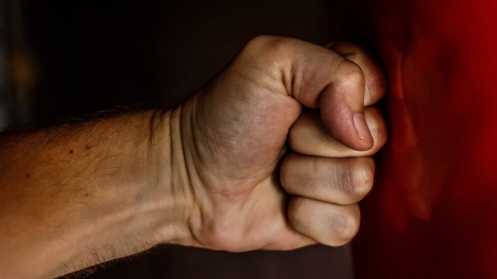 Close-up of a clenched fist against a dark background with a red fabric edge on the right side.
