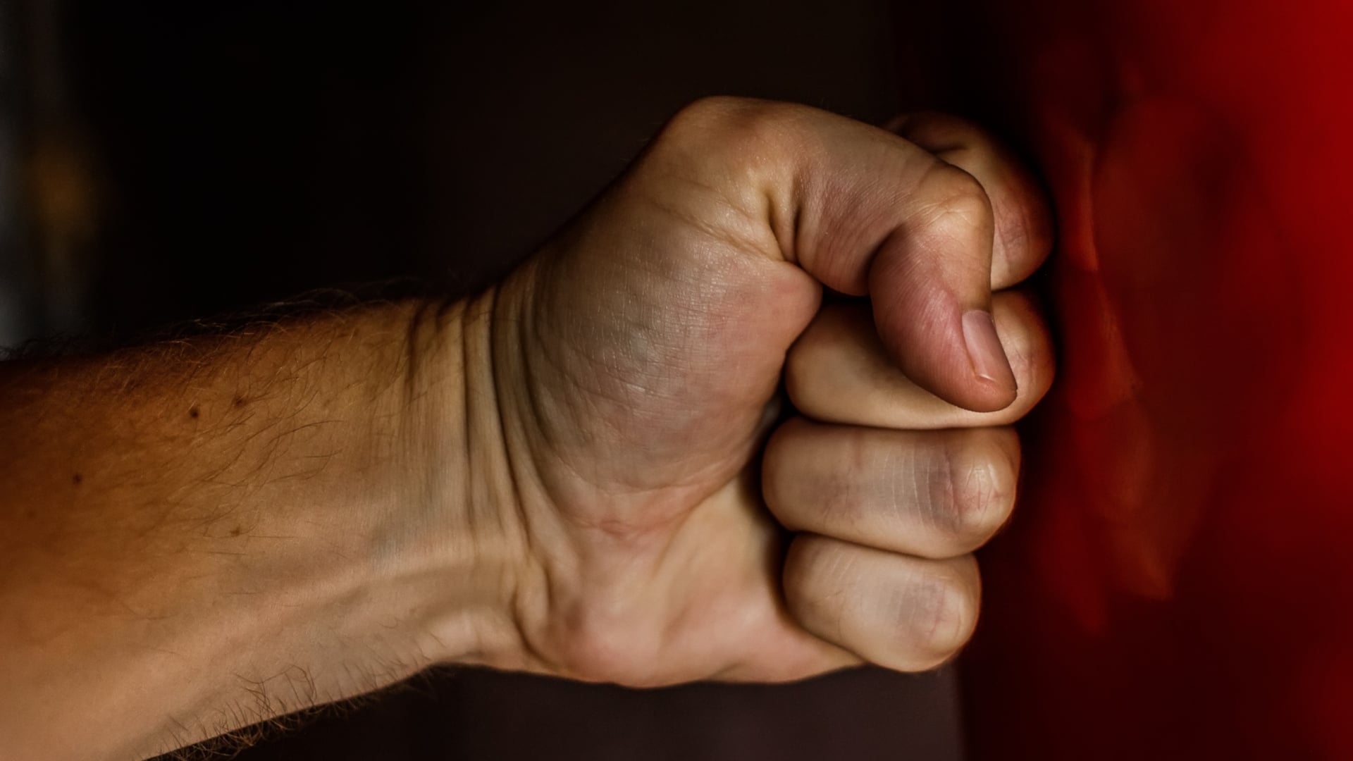 Close-up of a clenched fist against a dark background with a red fabric edge on the right side.