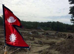 Zalany teren, za nim las, z przodu flaga Nepalu