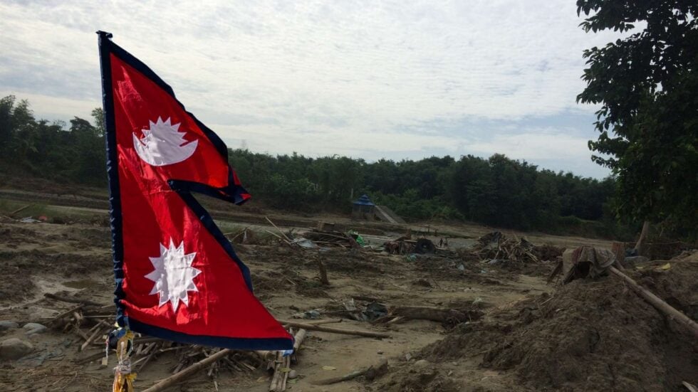 Zalany teren, za nim las, z przodu flaga Nepalu