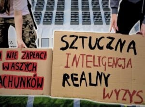Dwie kartonowe tablice z protestu w Piasecznie, na jednej napis „AI nie zapłaci waszych rachunków”, na drugiej „Sztuczna inteligencja, realny wyzysk”