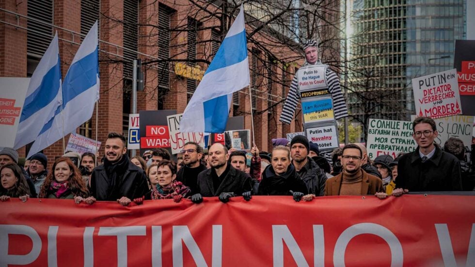 Maszerujący tłum z wielkim czerwonym banerem na przodzie, powiewają flagi rosyjskiej opozycji antywojennej (biało-niebiesko-białe), na przodzie idzie Julia Nawalna