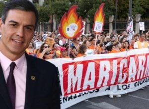 Tłum protestujących niesie wielki baner z imieniem Maricarmen, niektórzy trzymają tekturowe płomienie, z lewej strony doklejony Pedro Sanchez