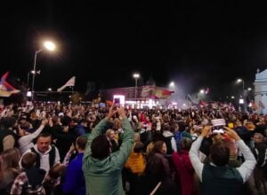 Tłum protestujący nocą, nad nim widać wiele powiewających flag Serbii